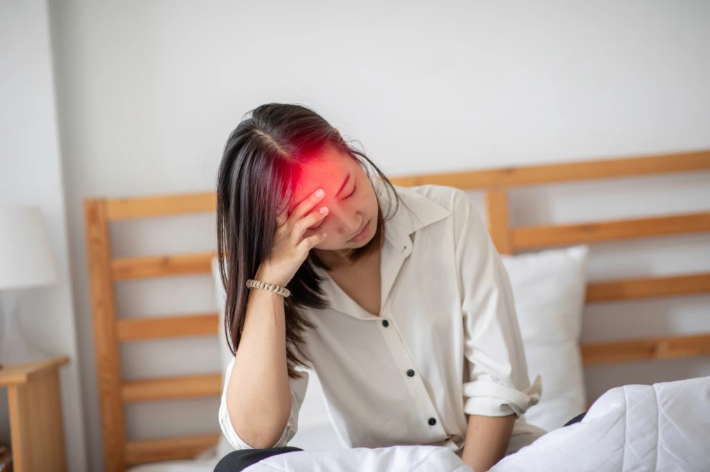 Woman holding her forehead with visible head pain, illustrating migraine symptoms requiring neurological evaluation.