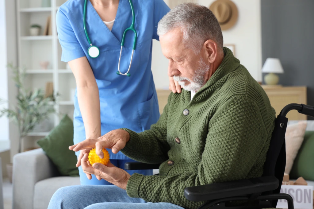 Healthcare professional assisting an older adult with hand therapy during Parkinson's disease rehabilitation.