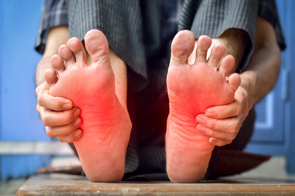 Person holding both feet with highlighted burning pain, illustrating symptoms of peripheral neuropathy requiring neurological evaluation.