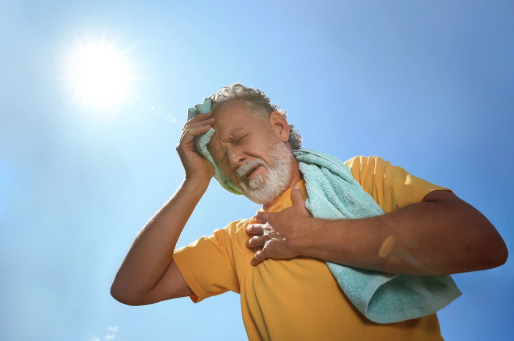 Older man holding his head and chest under bright sunlight, illustrating warning signs that may require urgent neurological evaluation.